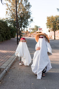 Trendy sheet ghosts costumes on little kids standing on a suburbs street. happy halloween holiday