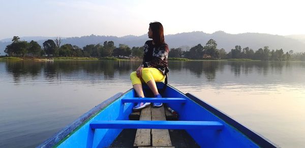 Woman looking away while sitting on boat in lake against sky