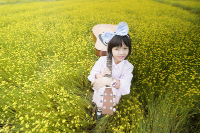 Portrait of cute girl with guitar standing on field