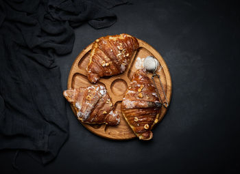 Baked croissants on a black wooden board sprinkled with powdered sugar, top view