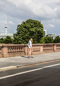 Full length of woman skateboarding on road in city against sky