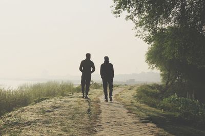 Rear view of men walking on sidewalk against sky