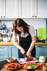 A young attractive girl in an apron prepares carpaccio in the home kitchen.