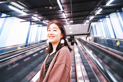 Portrait of smiling young woman on escalator at railroad station