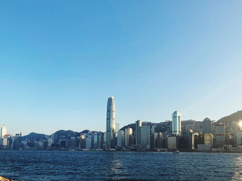 Sea and buildings in city against clear blue sky