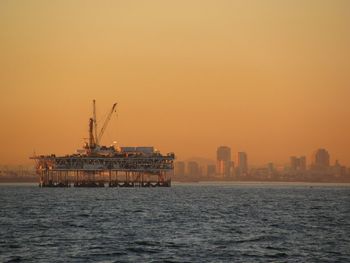 Offshore platform amidst sea against orange sky