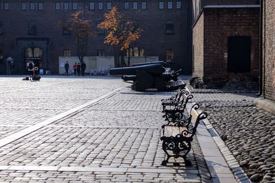 People on square by building in fortress with benches and cannons