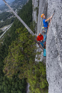 Two men rock climbing while belaying from hanging tree on exposed wall