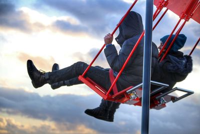 People sitting in chain swing ride against cloudy sky