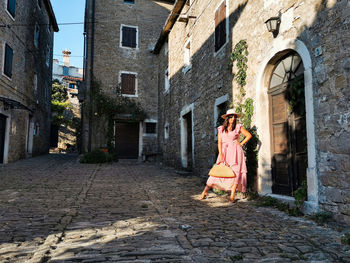 Young woman in pink dress in square of old town, stone buildings, fashion, lifestyle, travel.