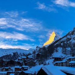 Snow covered houses by buildings against blue sky