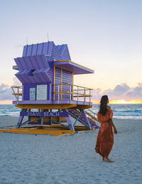 Rear view of woman sitting on beach against sky