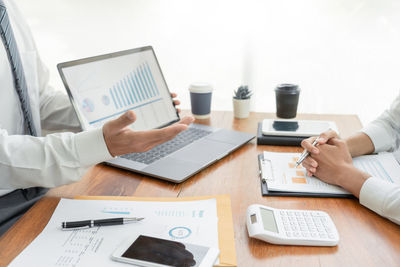 Midsection of businessman and colleague working on table