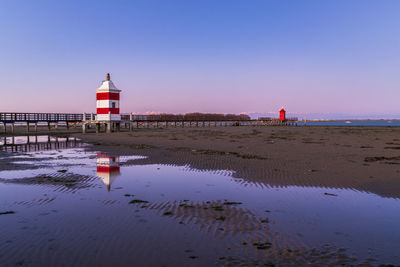 Lighthouse on beach by sea against clear sky