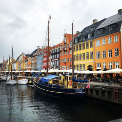 Boats moored in canal by buildings against sky