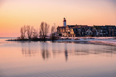 Scenic view of lake by buildings against sky during sunset