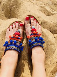 Low section of woman wearing traditional slippers on sand