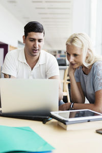 Male and female university students using laptop together at library