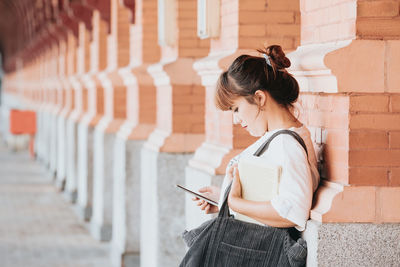 Side view of young woman standing against building