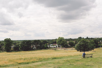 Rear view of man sitting on bench against cloudy sky