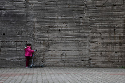 Full length of woman standing on footpath against wall