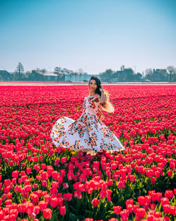 Woman standing by red flowering plants against sky