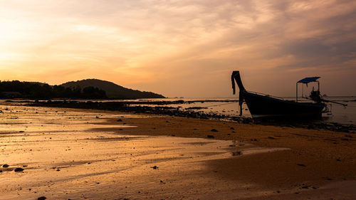 Fishing boat on beach against sky during sunset