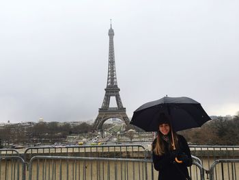 Young woman holding umbrella standing against eiffel tower in city during winter