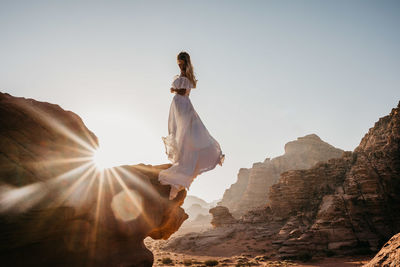 Woman in dress standing on rock against sky