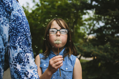 Portrait of girl blowing dandelion while standing in lawn