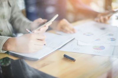 Midsection of colleagues using phone while working on office table