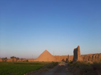 Road amidst field against clear blue sky