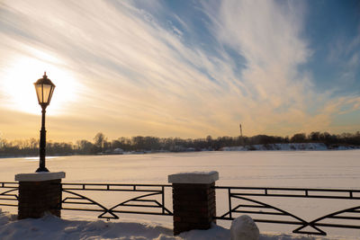 Snow covered railing against sky during sunset