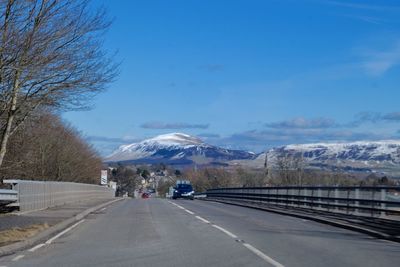 Road by mountains against sky during winter