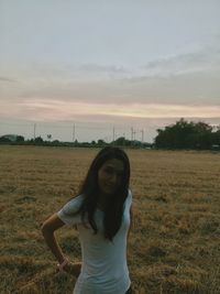 Woman standing on field against sky during sunset