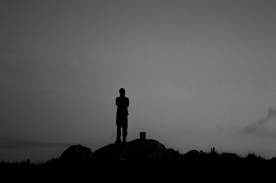 Rear view of silhouette man standing on rock against sky