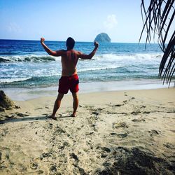 Rear view of shirtless man standing on beach against sky