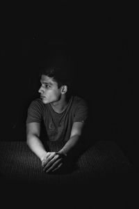 Man looking away while sitting at table in darkroom