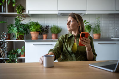 Thoughtful woman drinking tea during work break, looking at window, planning future working process