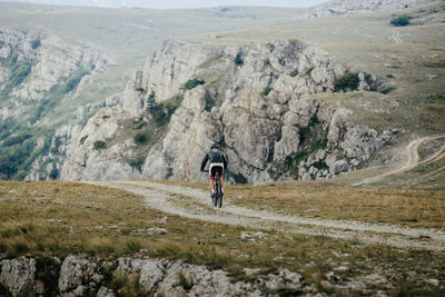 Rear view of man walking on rocks against mountains