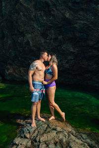 Young couple kissing while standing on rock by sea