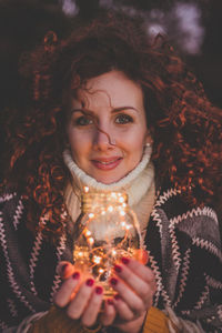 Portrait of young woman holding illuminated string lights in jar