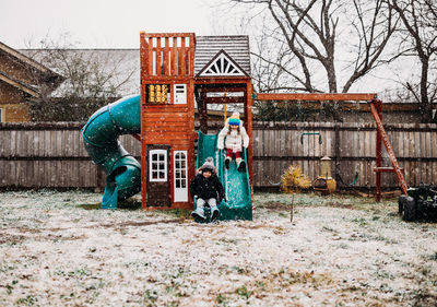 Young brother and sister sliding down swing set with falling snow