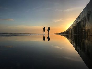 Silhouette people by sea against sky during sunset