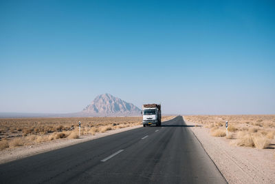 Road by desert against clear blue sky