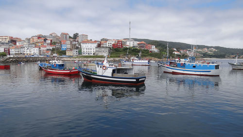 Sailboats moored on sea by city buildings against sky