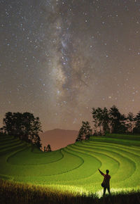 Rear view of man standing on field against sky at night