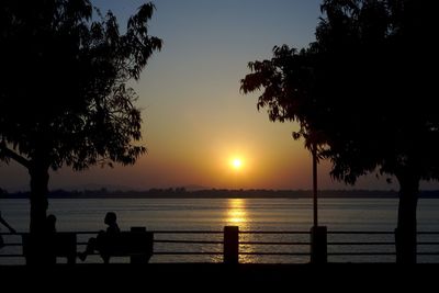 Silhouette of people sitting on bench at lakeshore