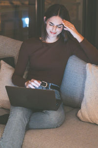 Young woman using phone while sitting on sofa at home