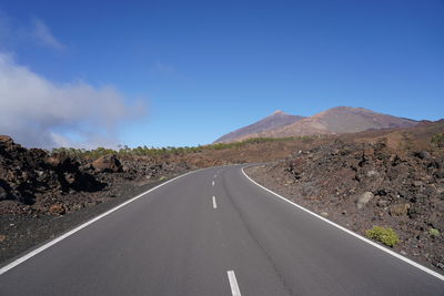 Road leading towards mountains against blue sky